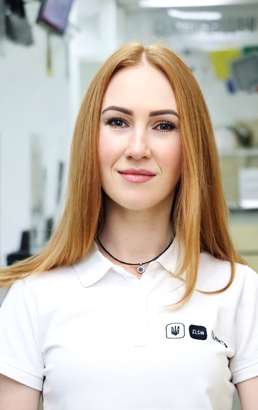 Жінка з рудим волоссям і підвіскою у футболці, усміхається.
